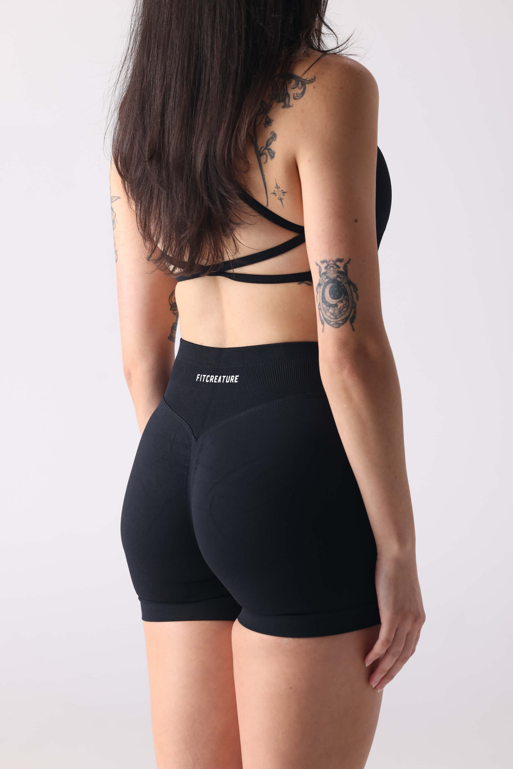 Person wearing black athletic shorts with a visible brand logo on a plain background