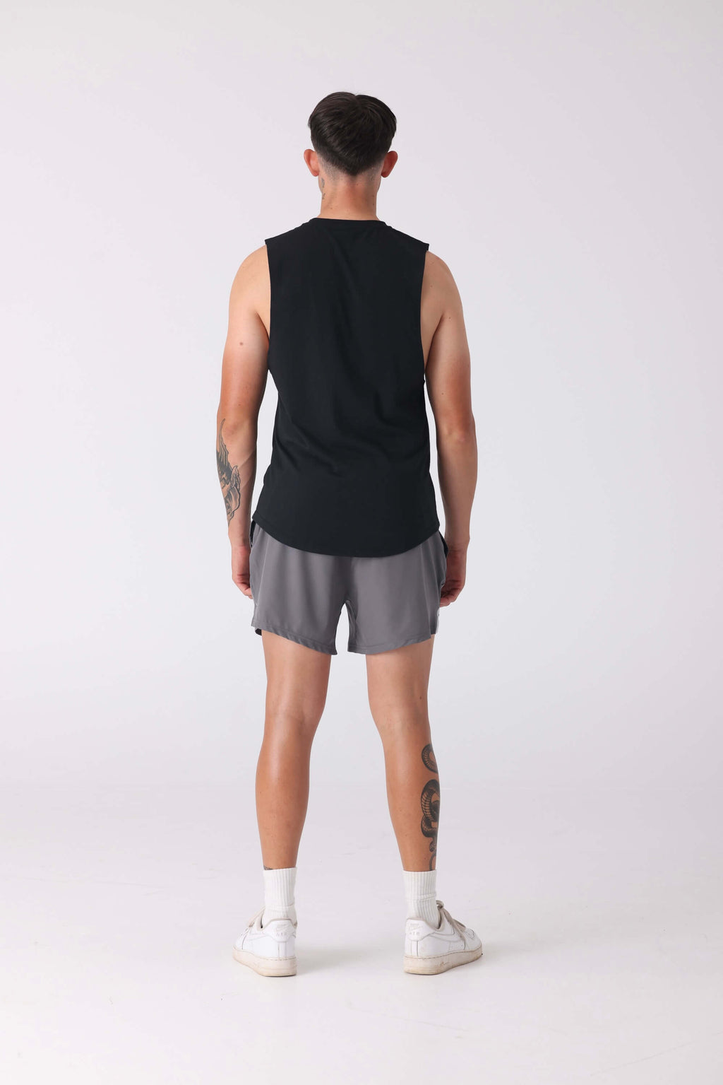 Person wearing a black sleeveless shirt and gray shorts on a white background