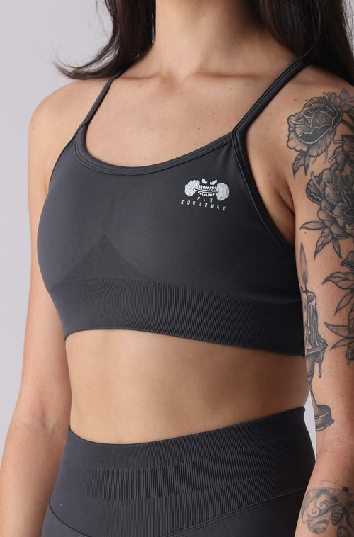Woman wearing a grey sports bra and leggings with a visible brand logo on a plain background
