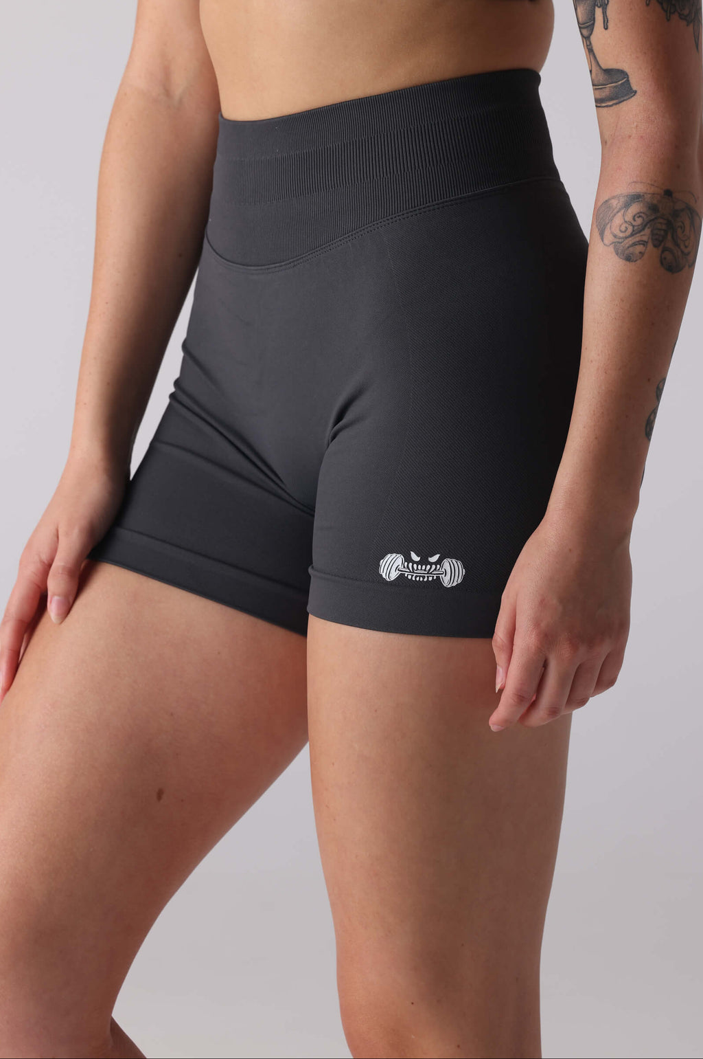 Person wearing grey athletic shorts and sports bra with visible branding on a plain background