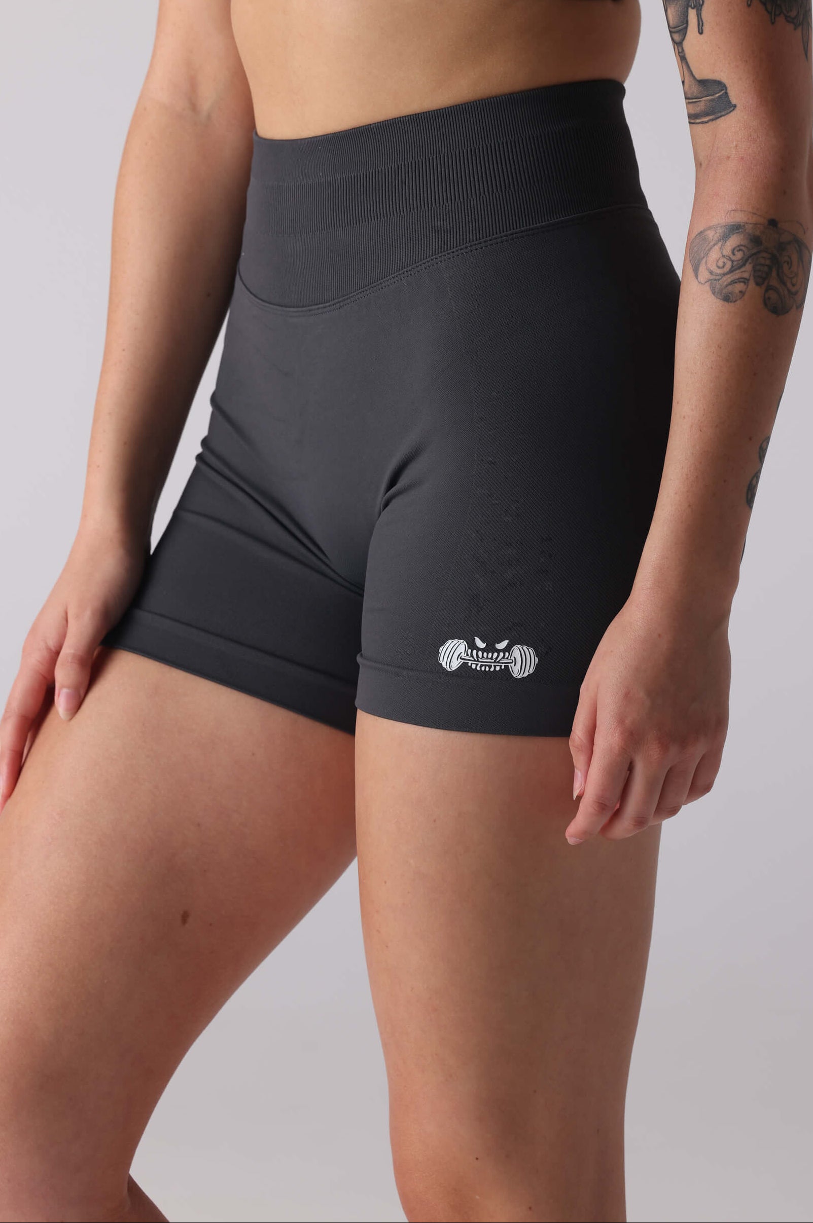 Person wearing grey athletic shorts and sports bra with visible branding on a plain background